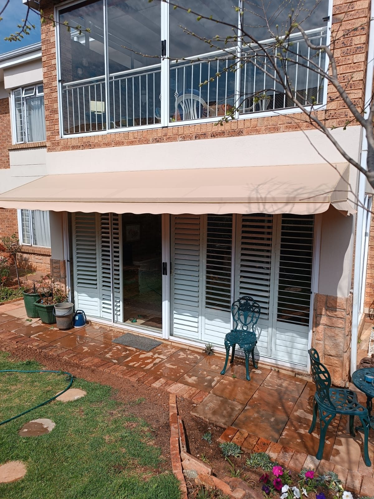 Folding-arm awning with plantation shutters behind